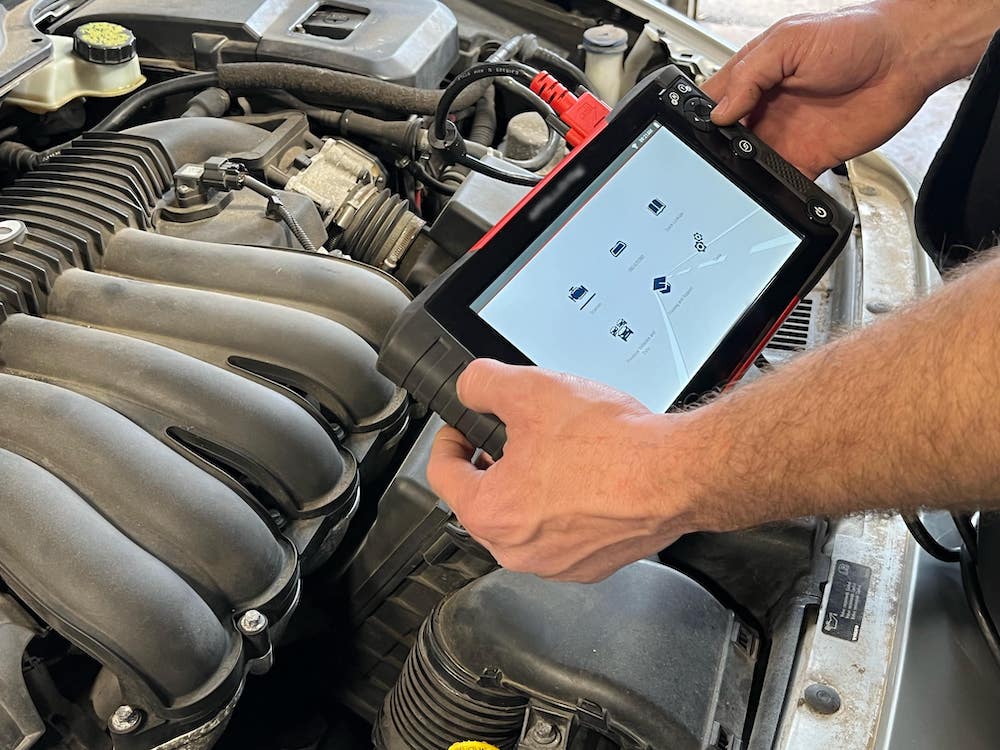 Technician using diagnostic tablet on vehicle engine bay