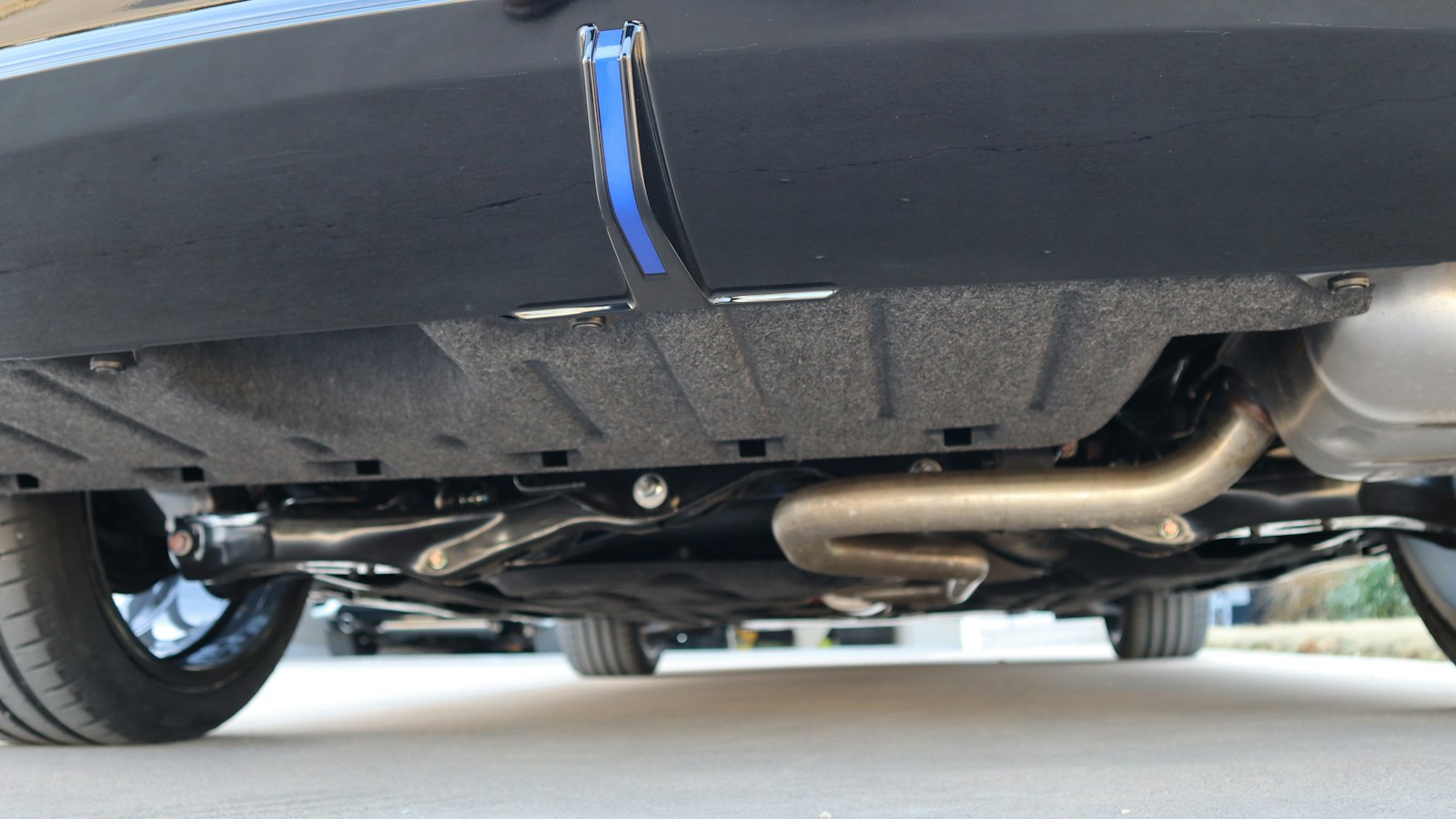 Underside of a car's rear end showing the exhaust pipe curving over the rear suspension into the muffler, the section an axle-back or cat-back exhaust replaces