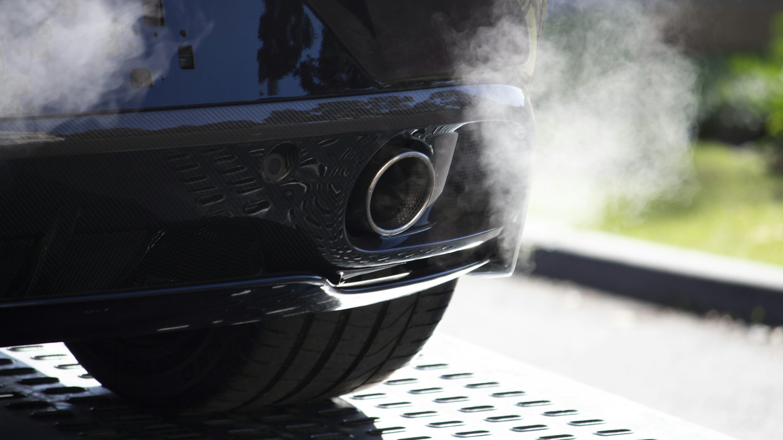 Exhaust vapor drifting from the tailpipe of a car on a shop lift, where catalytic converter efficiency is checked