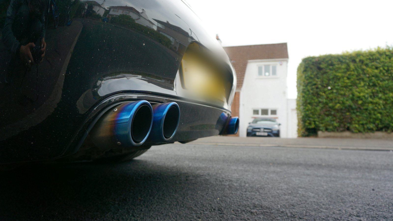 Dual heat-blued exhaust tips under the rear bumper of a dark sedan, the visible end of a cat-back vs axle-back exhaust upgrade