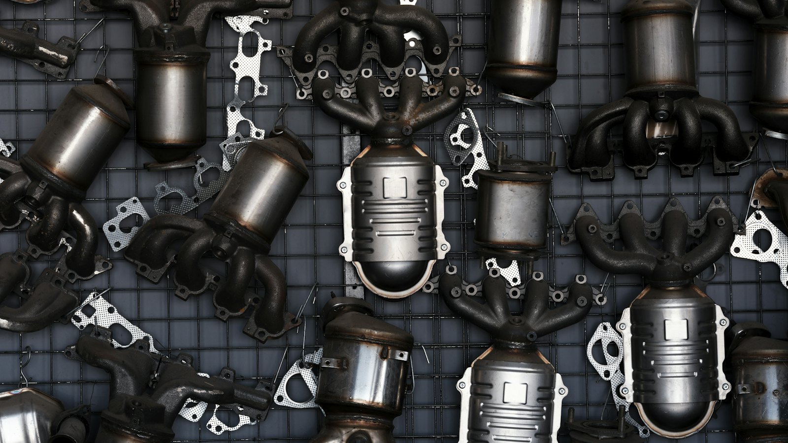 Rows of catalytic converters and exhaust manifolds hanging on a parts wall, the part behind most of a catalytic converter replacement cost