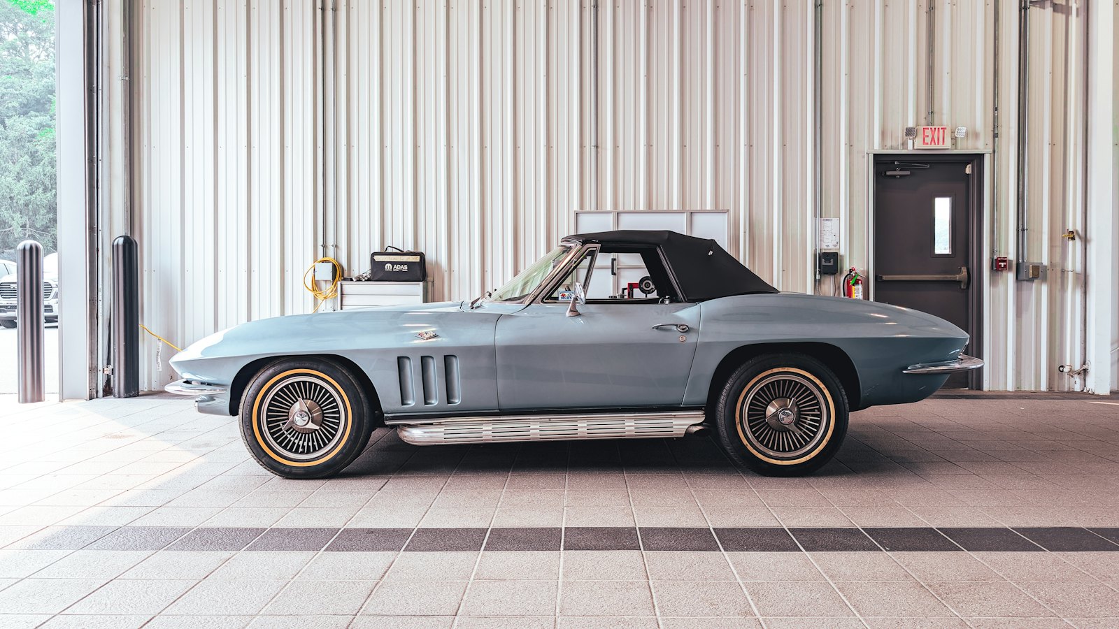 Classic blue convertible with its soft top up, parked on a clean floor inside a large garage ready for winter storage