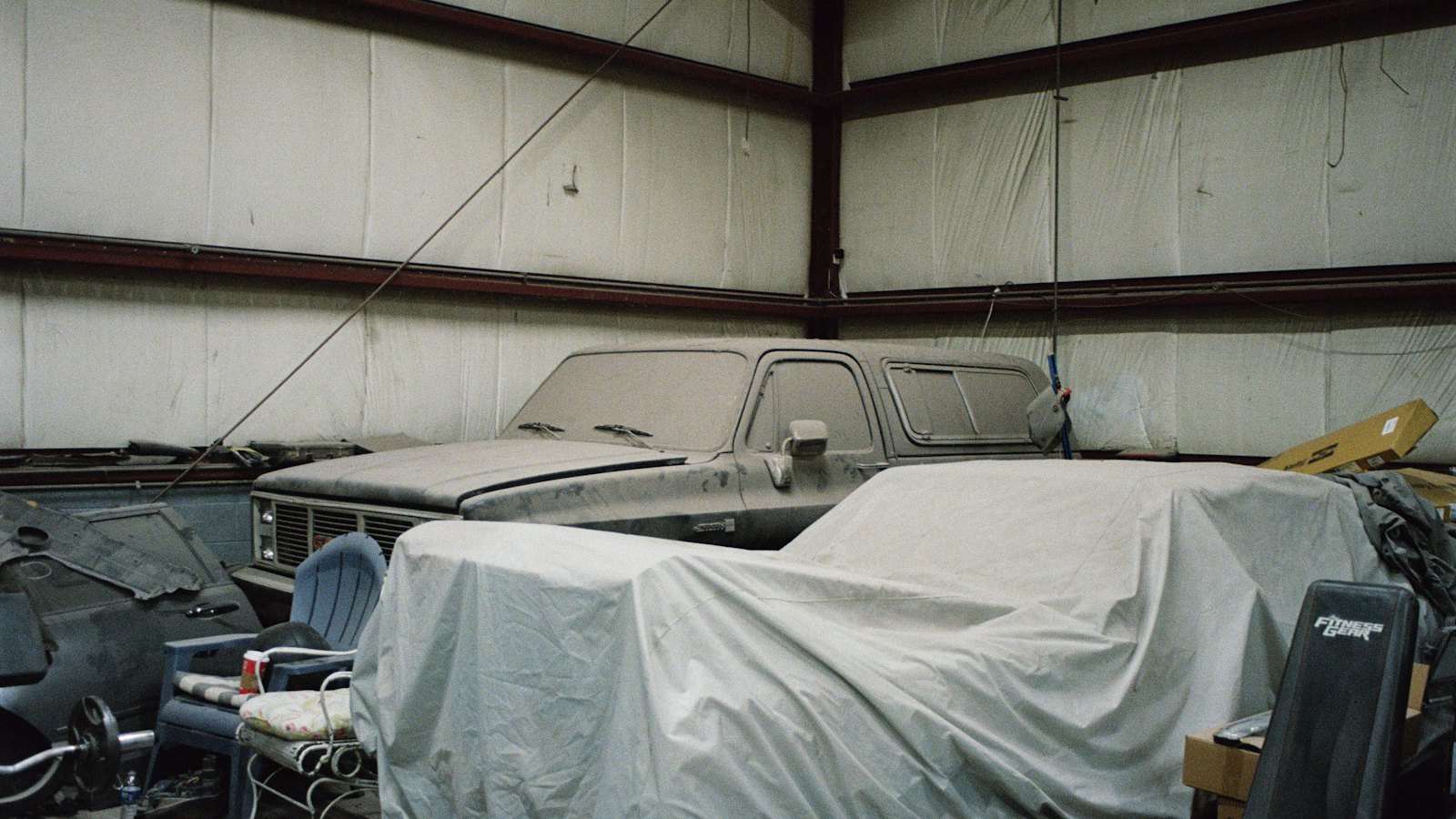Dust-covered pickup truck and a vehicle under a fabric cover stored inside a steel building for the winter