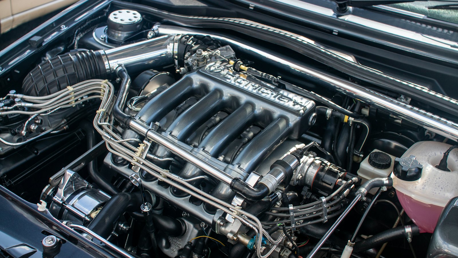 Open engine bay with a translucent coolant reservoir filled with pink coolant, one of the levels to check when a car is leaking fluid