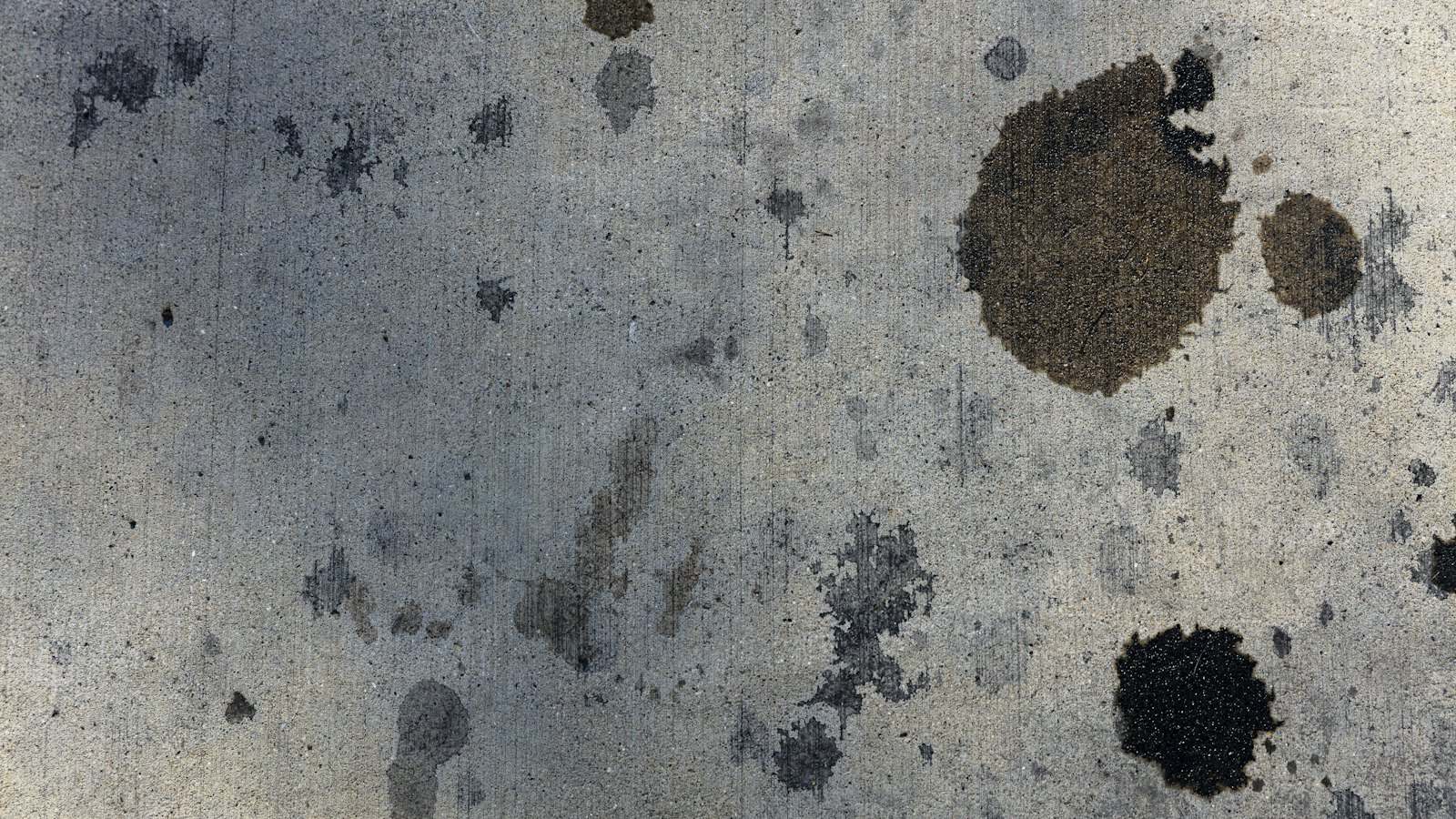 Dark oil spots on a concrete driveway, the first clue when you're asking what fluid is leaking from my car