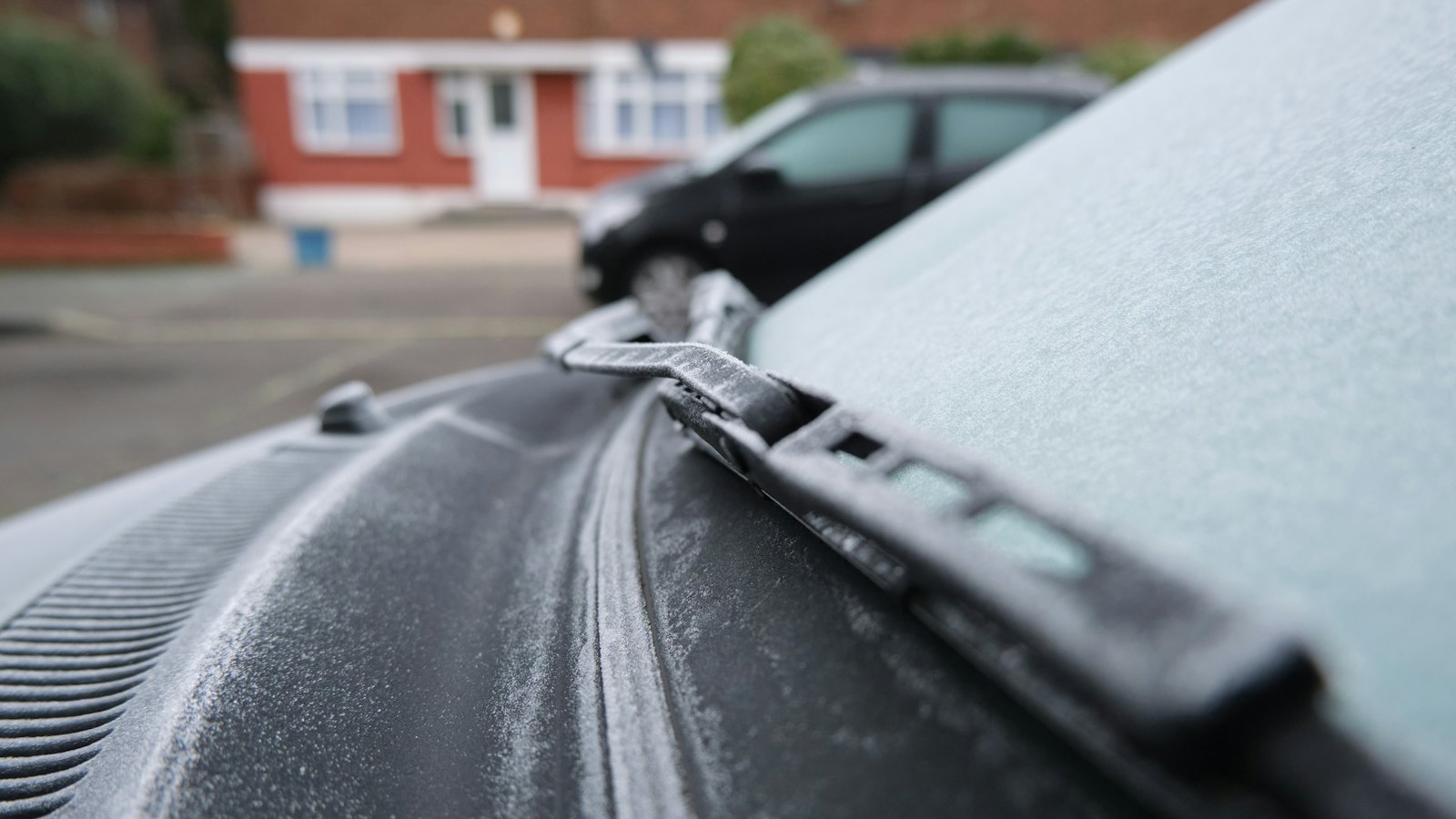 Frost covering a car's windshield and wiper blade on a cold morning, a reminder to check wipers before winter