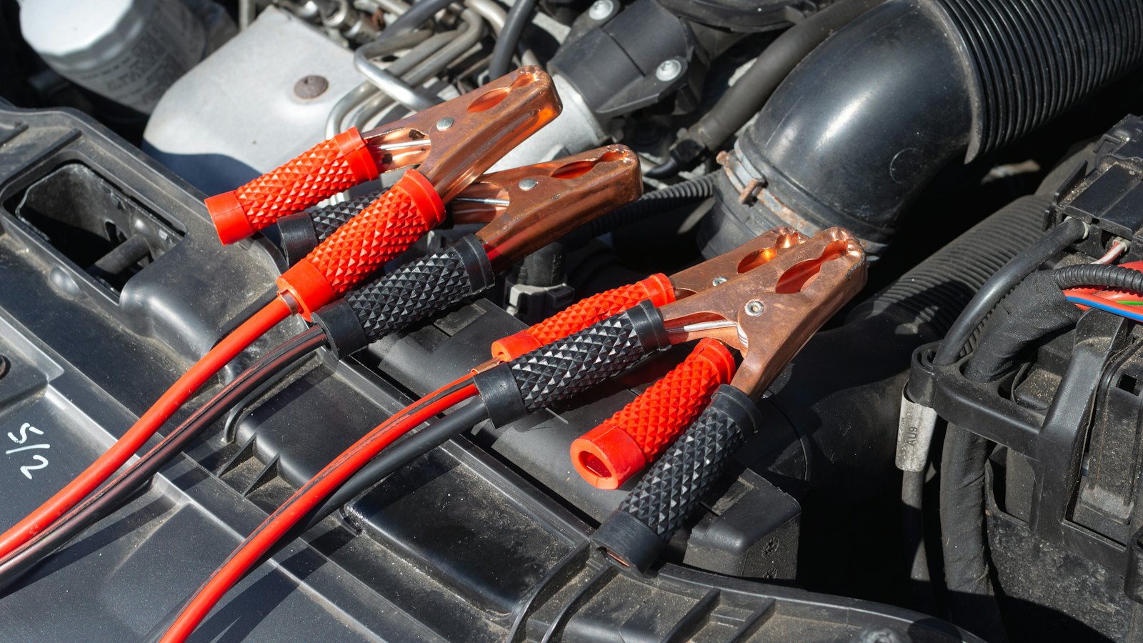 Red and black jumper cable clamps resting in an open engine bay after a jump start for a dead car battery