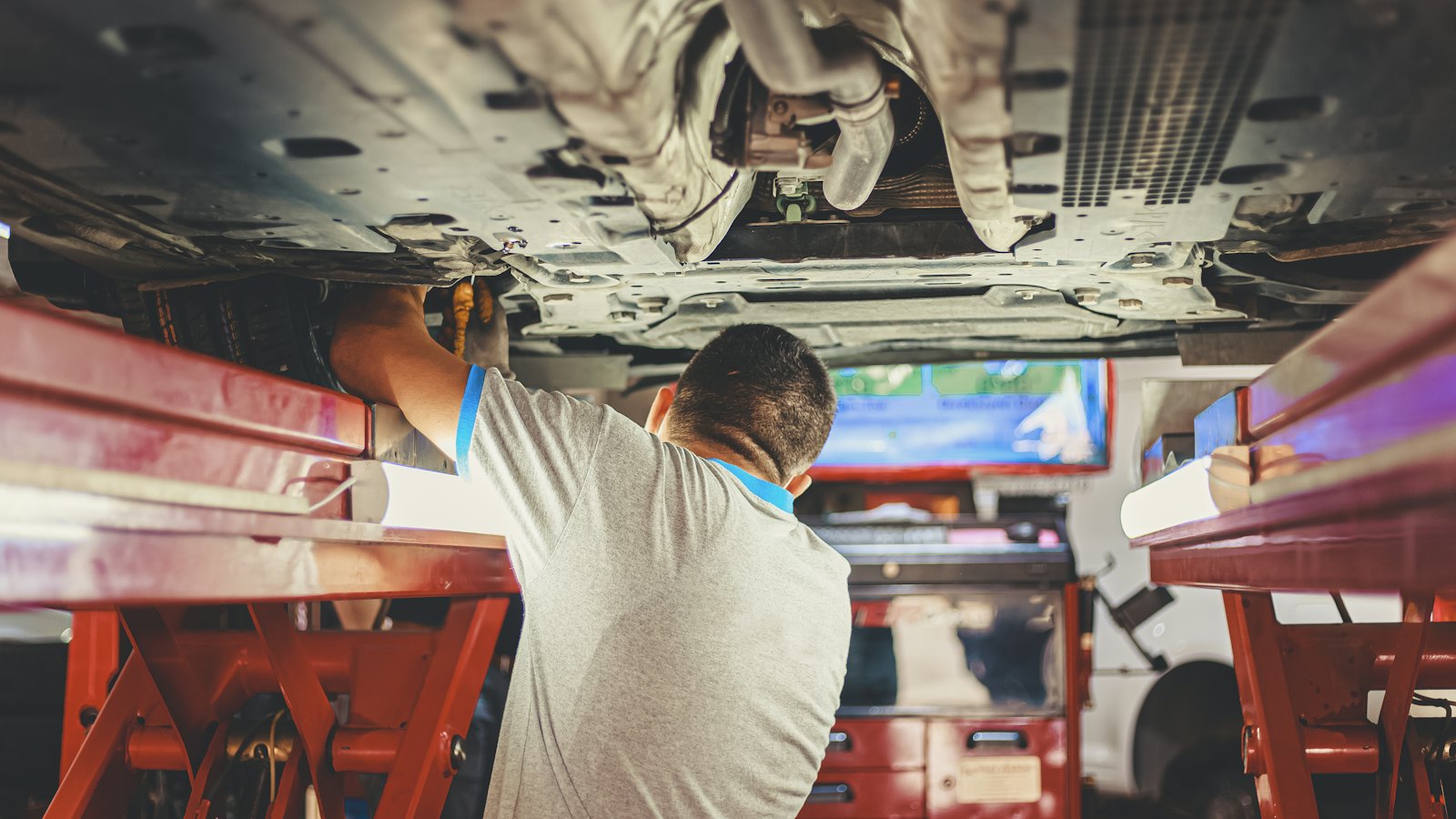 Technician inspecting the underside of a car raised on a lift, the kind of check NH car inspection in 2026 no longer requires