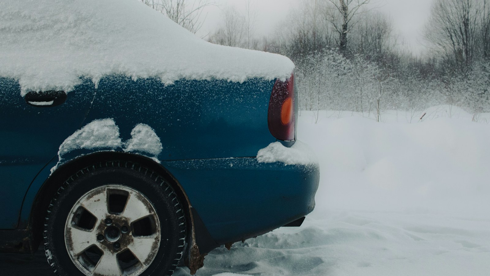 Blue sedan parked outside with snow on the roof and fender and around the rear wheel, the kind of overnight cold that lowers tire pressure