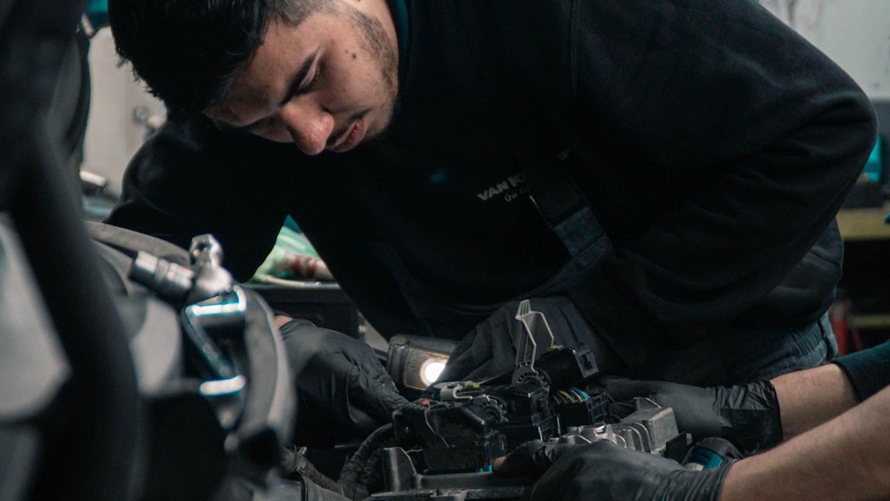 Technician inspecting under the hood of a car during a summer cooling-system and electrical check