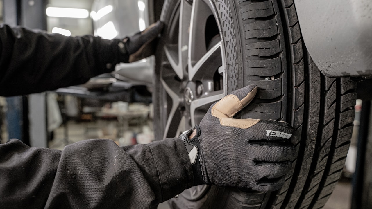 Gloved technician inspecting a car tire and tread at an auto shop in Derry, NH before summer driving
