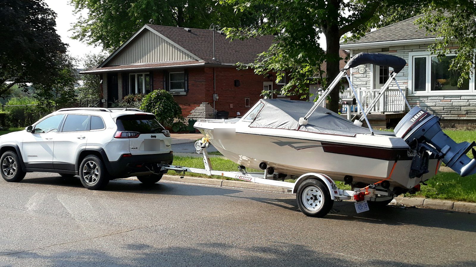 White SUV towing a small boat on a trailer down a residential street, the kind of load that heats up transmission fluid once towing season starts