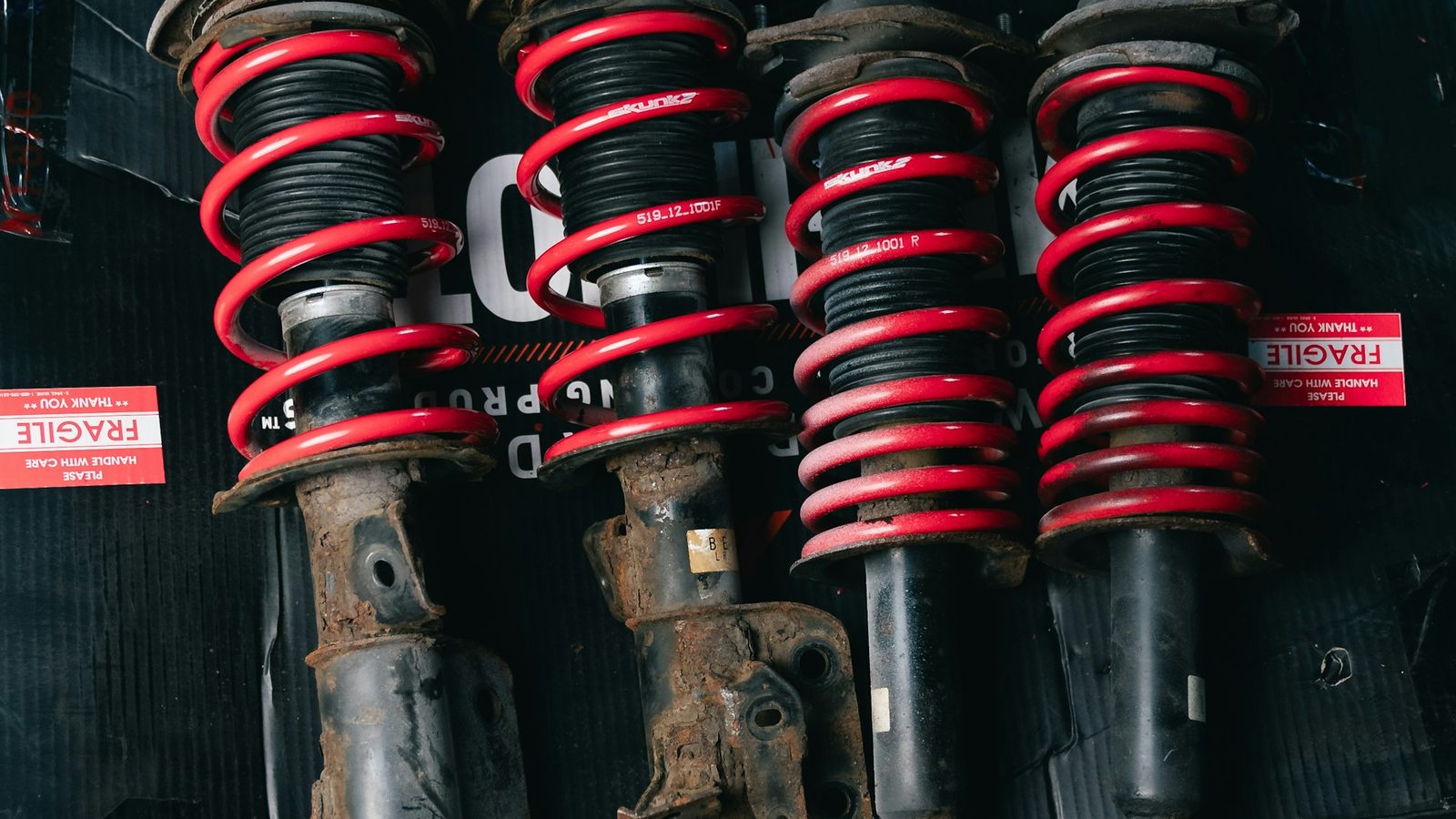 Two rusted high-mileage struts removed from a New Hampshire commuter car next to two new replacement strut assemblies